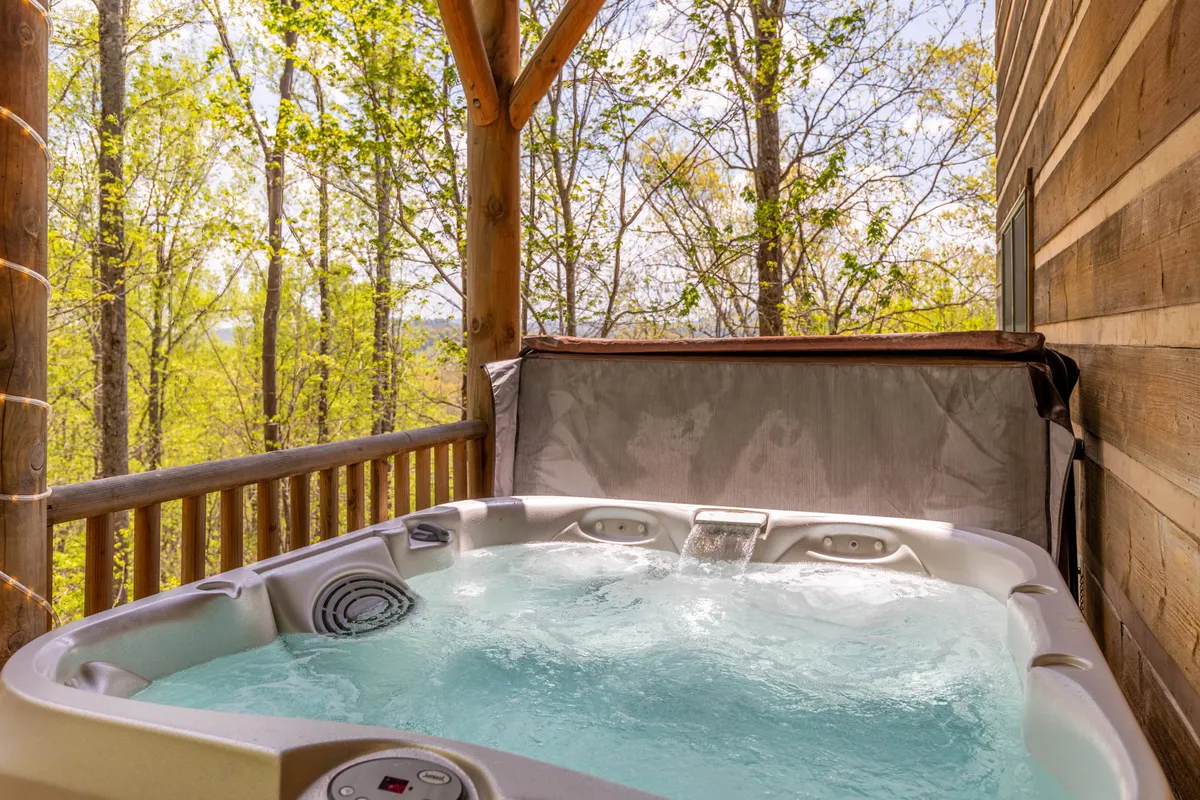 This image captures a spacious deck with a bubbling hot tub surrounded by trees and expansive views of the landscape, inviting guests to relax and soak in the natural beauty.