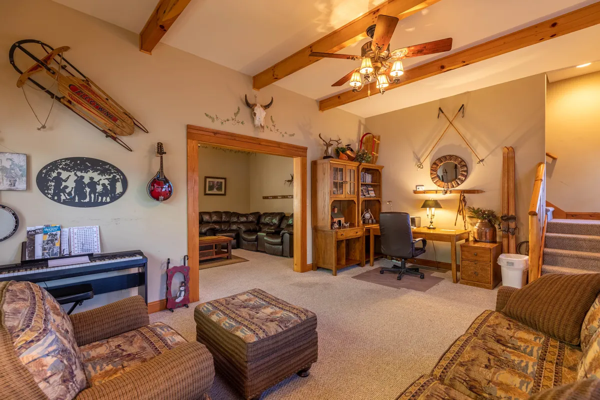 This interior image highlights a room with wooden beams, musical instruments, a home office setup, and comfortable seating. Visible are both creative tools and cozy touches, suggesting a space designed for jam sessions, writing, or relaxing in a music-themed environment.