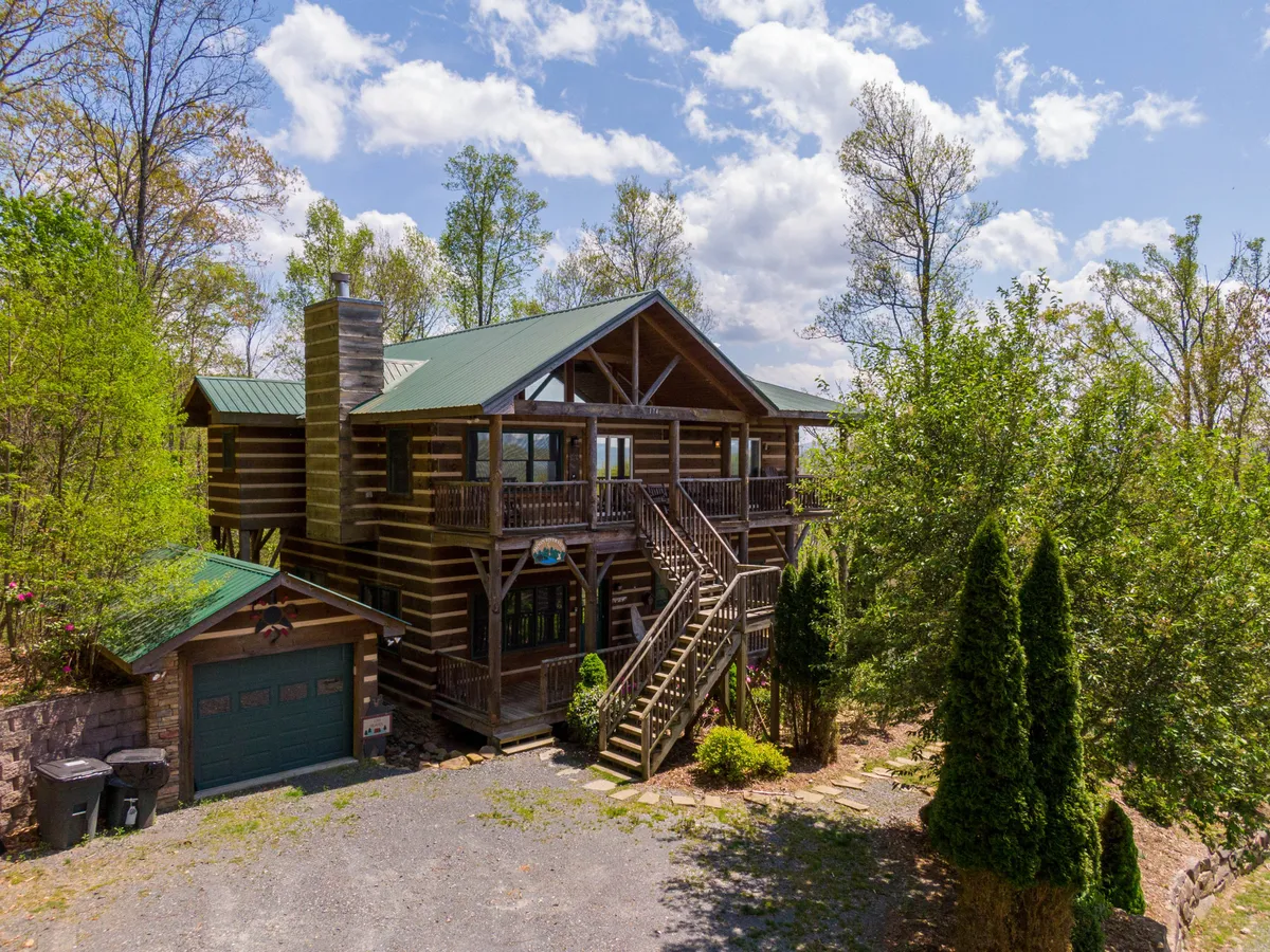 This image showcases the log cabin structure surrounded by lush green foliage, with a staircase leading to the entrance. The porch area and natural setting invite guests to enjoy the outdoors and provide ample space for pets to explore safely.