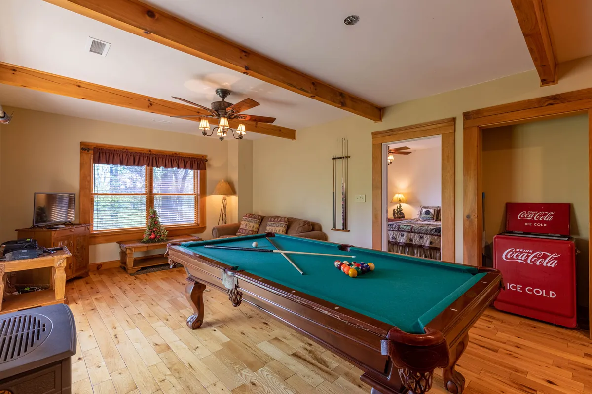 This casual and friendly space features a pool table, a Coca-Cola cooler for drinks, comfortable seating, and windows that let in abundant natural light. The wooden beams and rustic decor emphasize a laid-back, family-friendly atmosphere ideal for game nights or relaxing after a day outdoors.
