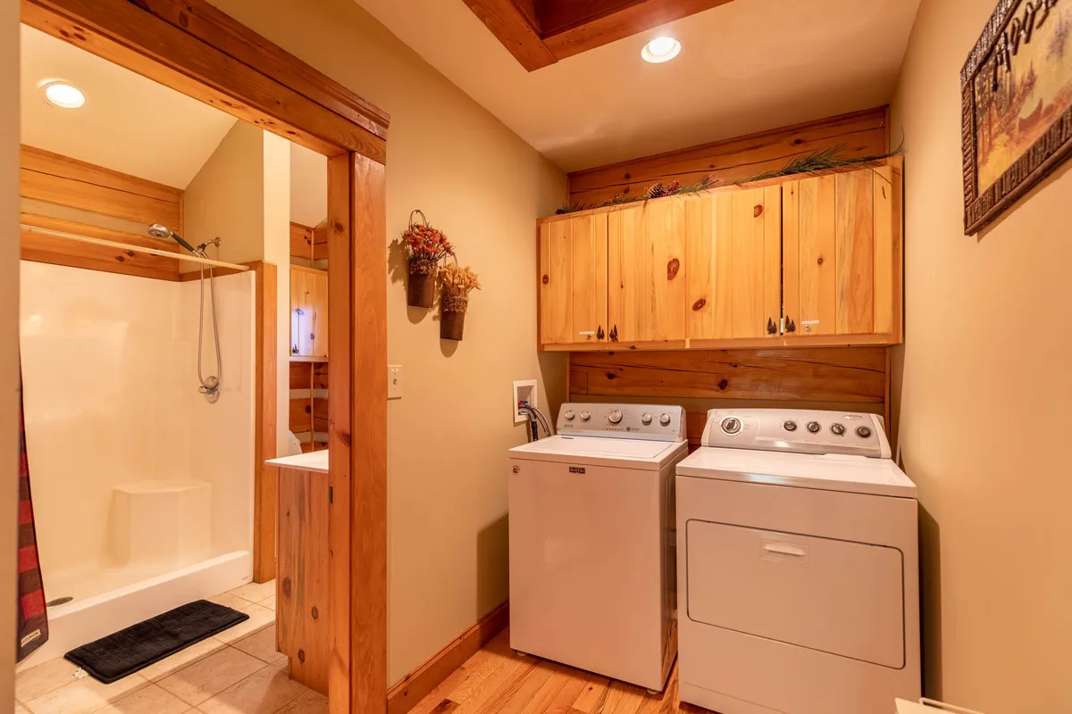 A practical laundry area featuring a washing machine and dryer set next to a shower area, with wood cabinetry for storage. The space is designed for easy access to laundry facilities during extended stays.