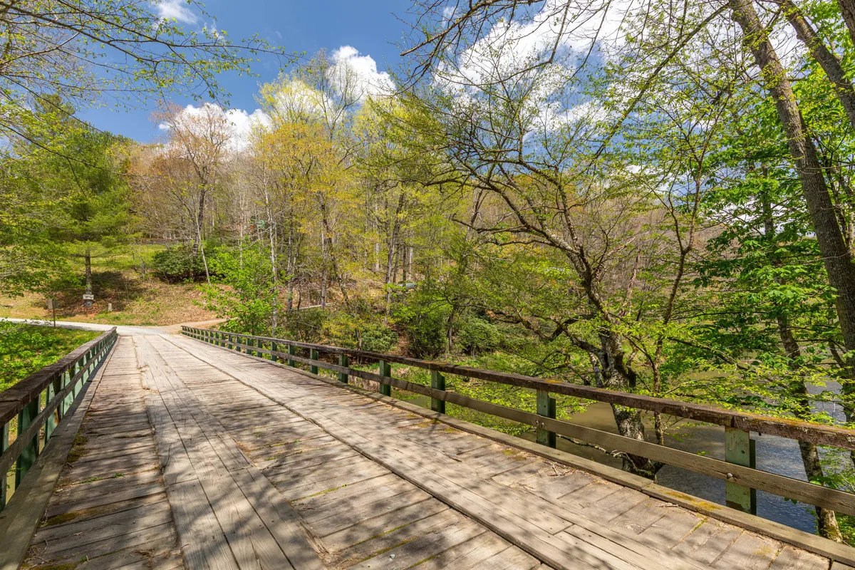 A serene wooden bridge crosses calm water surrounded by lush greenery and distant hills. The peaceful scene invites quiet walks, wildlife observation, and moments of reflection, illustrating easy access to outdoor activities.