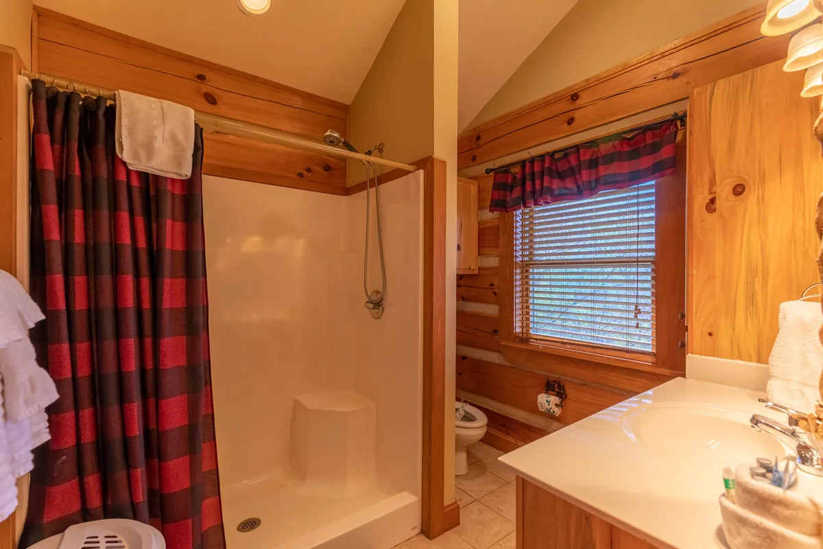 A modern bathroom with a tiled shower area, a vanity with a sink, and a window adorned with plaid curtains. The space is bright and functional, designed for convenience and comfort during both short and long stays.