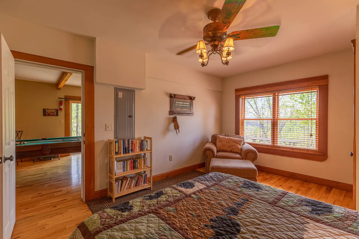 A tranquil bedroom scene with a bed topped with a patterned quilt, an armchair by the window, and a bookshelf brimming with books. Sunlight streams through the window, illuminating a perfect reading nook.